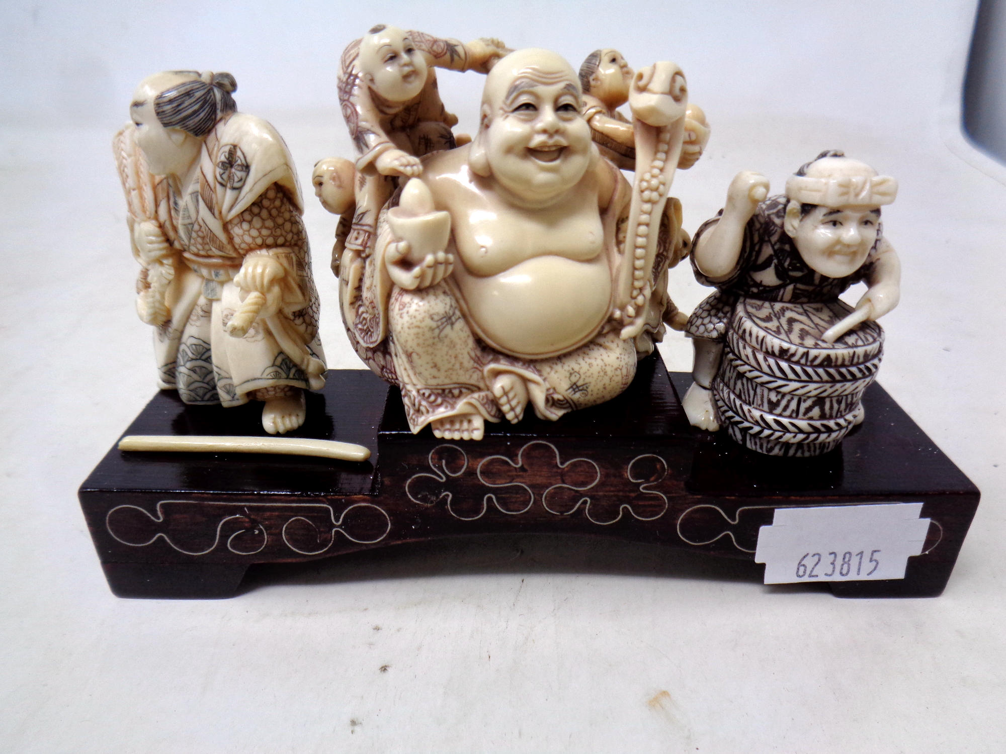 Three carved Japanese ivory and pen work netsuke on wooden stand together with a carved bone sword