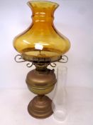 An antique brass oil lamp with amber glass shade and chimney