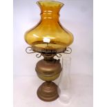 An antique brass oil lamp with amber glass shade and chimney