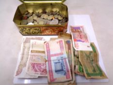 A tin containing a quantity of foreign currency, both coins and notes, from The Gambia, Jordan,