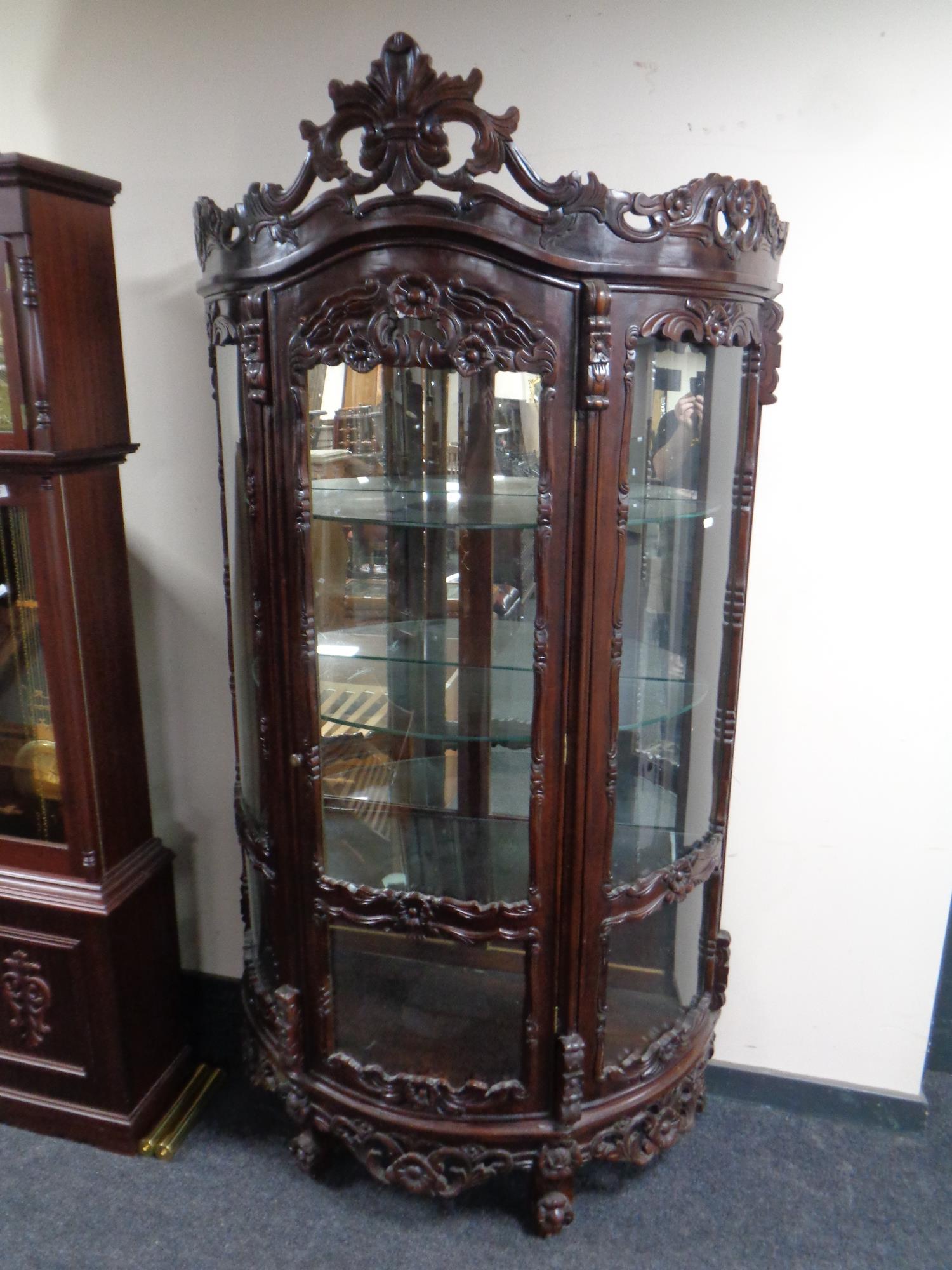 A reproduction ornately carved bowfronted display cabinet in a mahogany finish