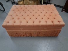 An oversized Ottoman foot stool upholstered in a pink fabric