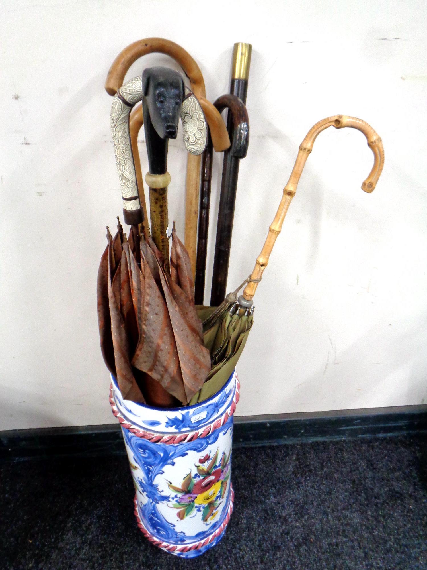 An Italian glazed ceramic stick stand containing vintage walking sticks and parasols