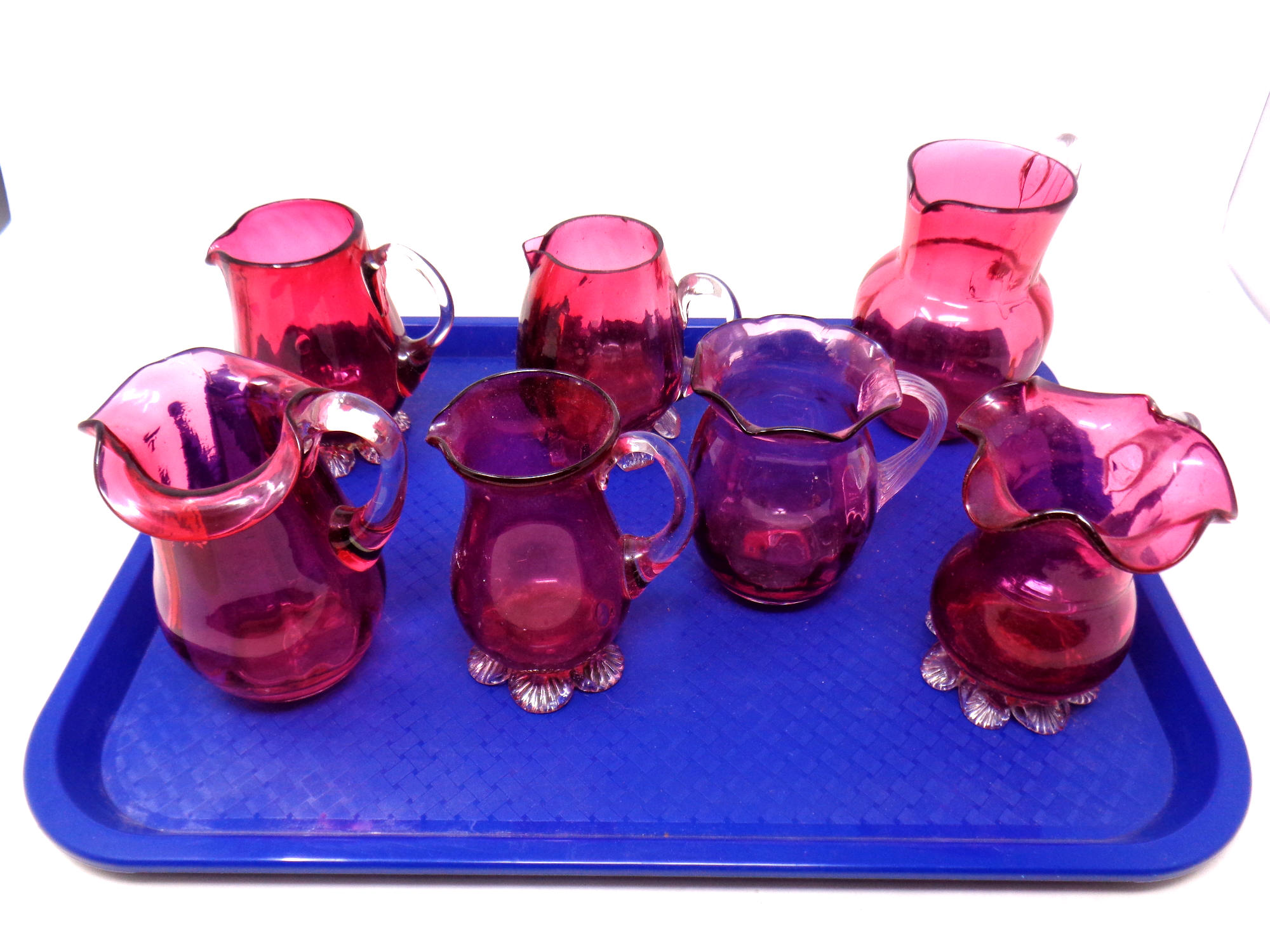 A tray containing seven antique cranberry glass jugs