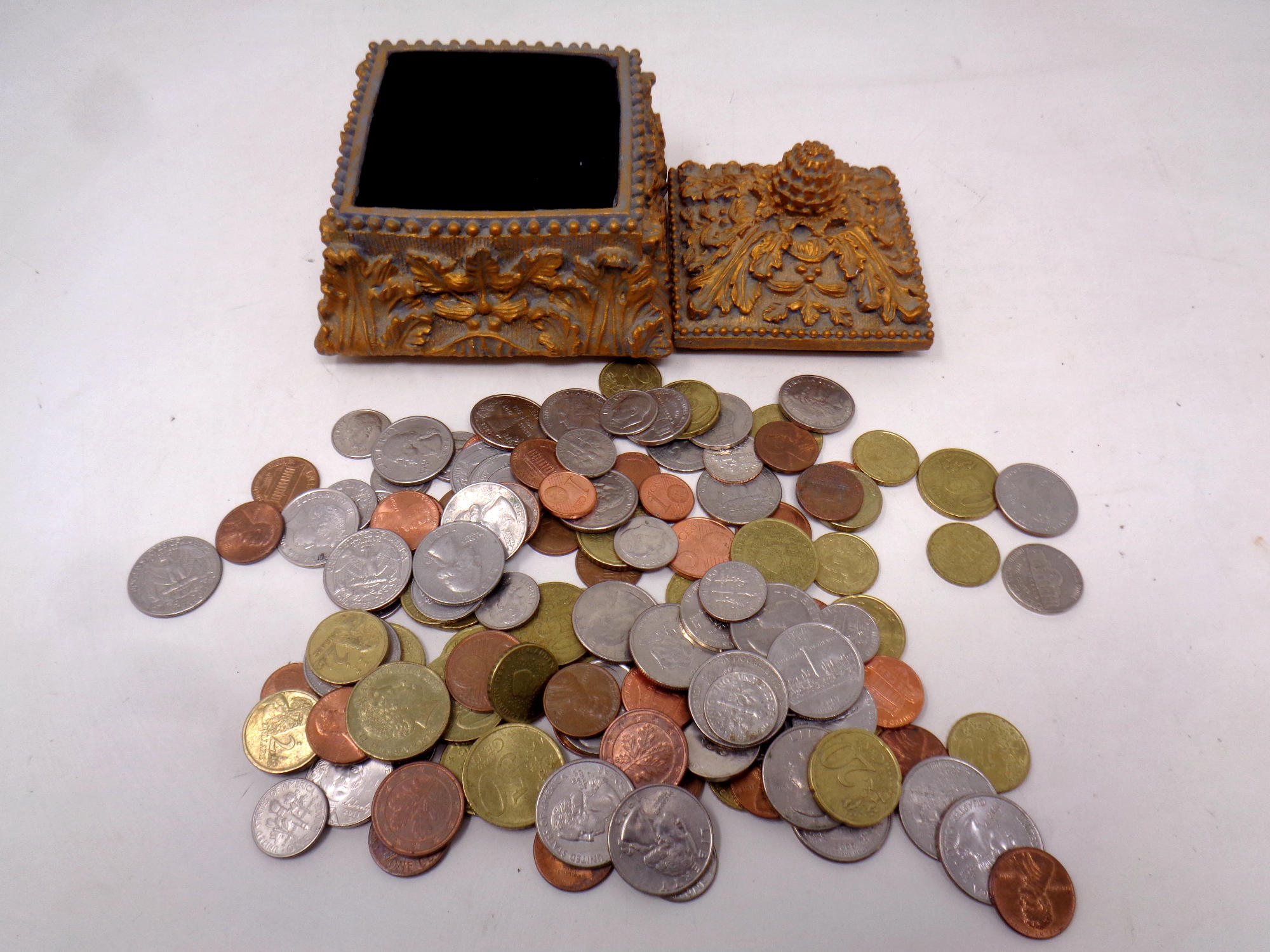 A decorative gilt lidded trinket box containing US and European coins