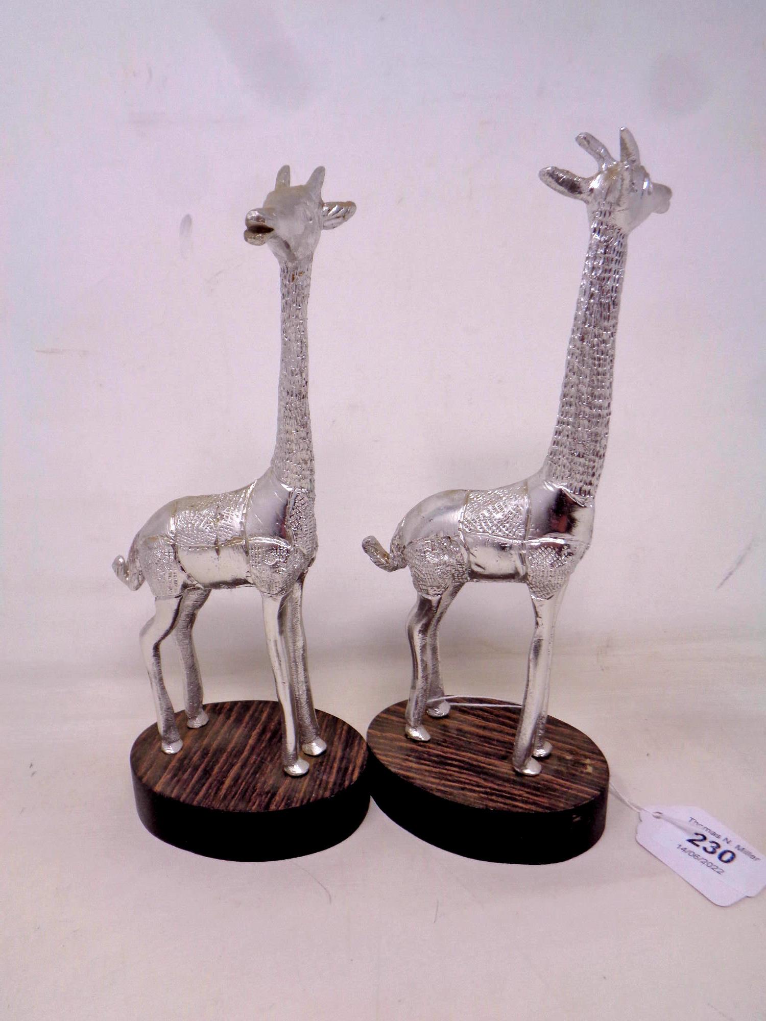 A pair of tin giraffe figures mounted on wooden plinths, height 23.5 cm.