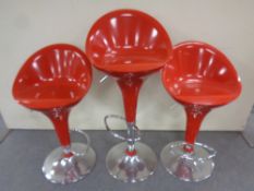 Three red plastic and chrome gas lift bar stools