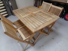 A slatted teak garden table on X-framed support, together with the four folding teak chairs.