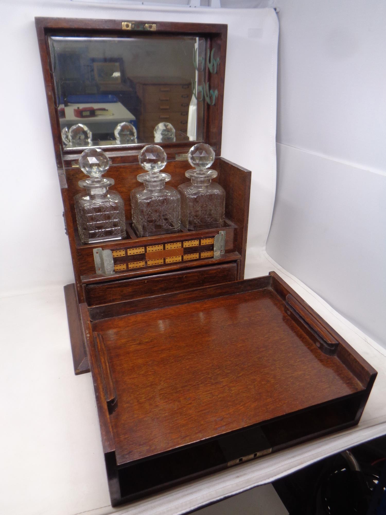A 19th century oak three-bottle decanter box containing internal drawers, cribbage board,