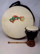 A Bodhran drum with beater in a carry bag together with a further African hand drum.