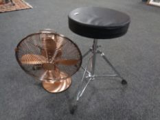 An adjustable drummer's stool on tripod stand and a retro style fan in a copper finish