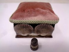 A silver and fabric pin cushion box decorated with silver shells containing a thimble (London