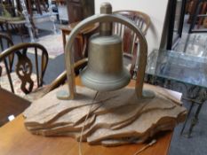 A brass bell mounted on a carved wooden plinth