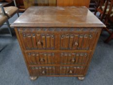 An oak linen fold three drawer chest on bun feet