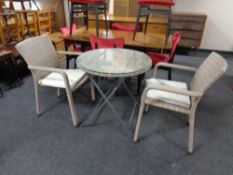 A contemporary wicker glass topped patio table and two matching armchairs