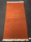 A fringed rug on orange ground 72 cm x 138 cm