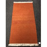 A fringed rug on orange ground 72 cm x 138 cm