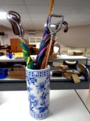 A blue and white glazed ceramic stick stand containing shooting sticks and umbrellas