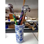 A blue and white glazed ceramic stick stand containing shooting sticks and umbrellas