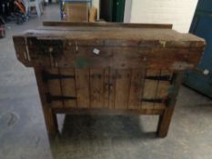 A vintage wooden work bench fitted with a vice and cupboards below