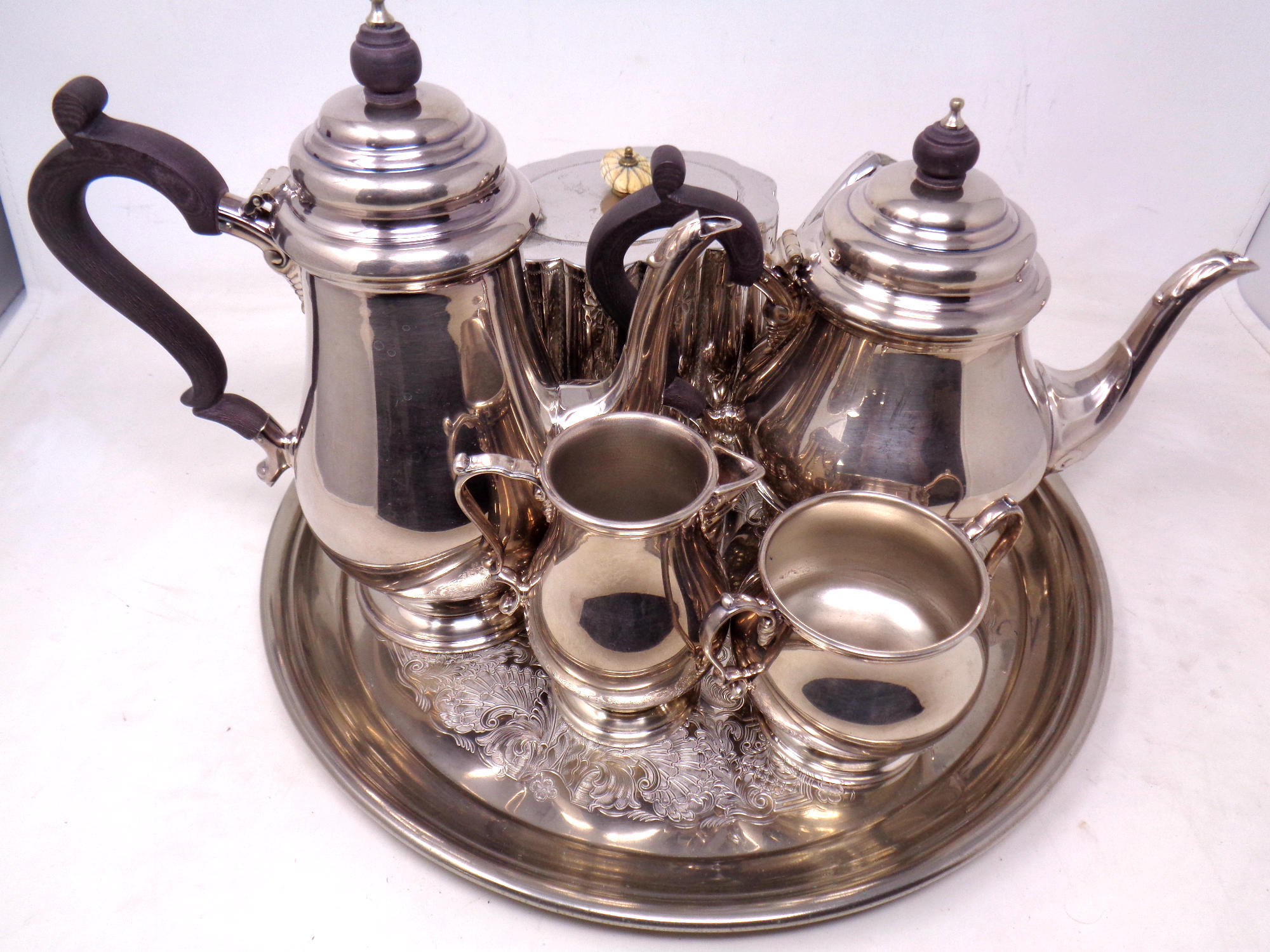 A plated circular tray containing a four piece silver plated tea service and further plated teapot