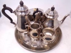 A plated circular tray containing a four piece silver plated tea service and further plated teapot