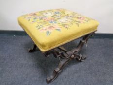 A Victorian embroidered footstool on carved X-frame support