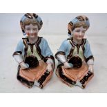 A pair of bisque nodding head figures modelled as seated gentlemen holding fans