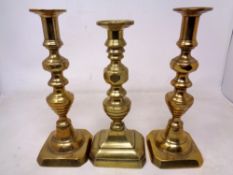 A pair of brass candlesticks together with another single example