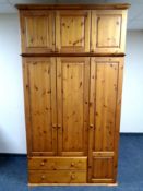 A pine triple door wardrobe fitted with drawers and top box
