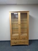 A contemporary light oak display cabinet with three drawers in the base.