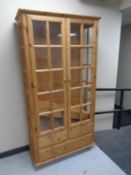 A pine double door glazed display cabinet fitted with three drawers