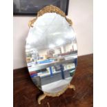 An oval frameless dressing table mirror on gilt wood stand.