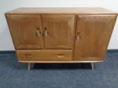 An Ercol elm and beech three door sideboard on raised legs (as found) CONDITION REPORT: