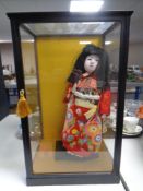 A Japanese porcelain headed doll in display case.