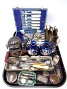 A tray containing a cast iron money box, assorted plated cutlery, a brass letter rack,