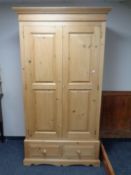 A stripped pine double door wardrobe fitted with two drawers.
