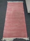 A pink fringed Chinese embossed rug.