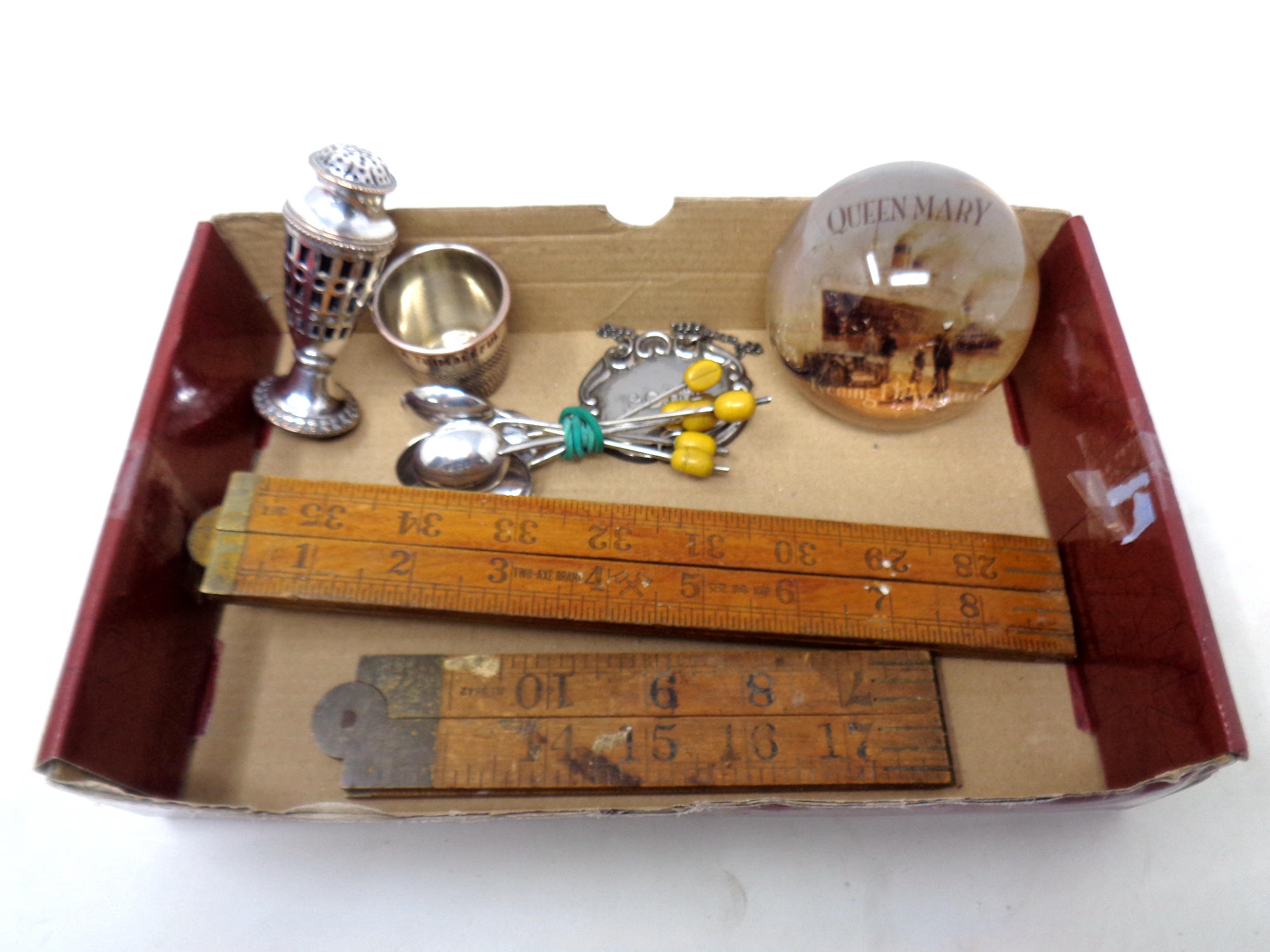 A box containing a Queen Mary paperweight, two folding boxwood rules, Art Deco plated teaspoons etc.