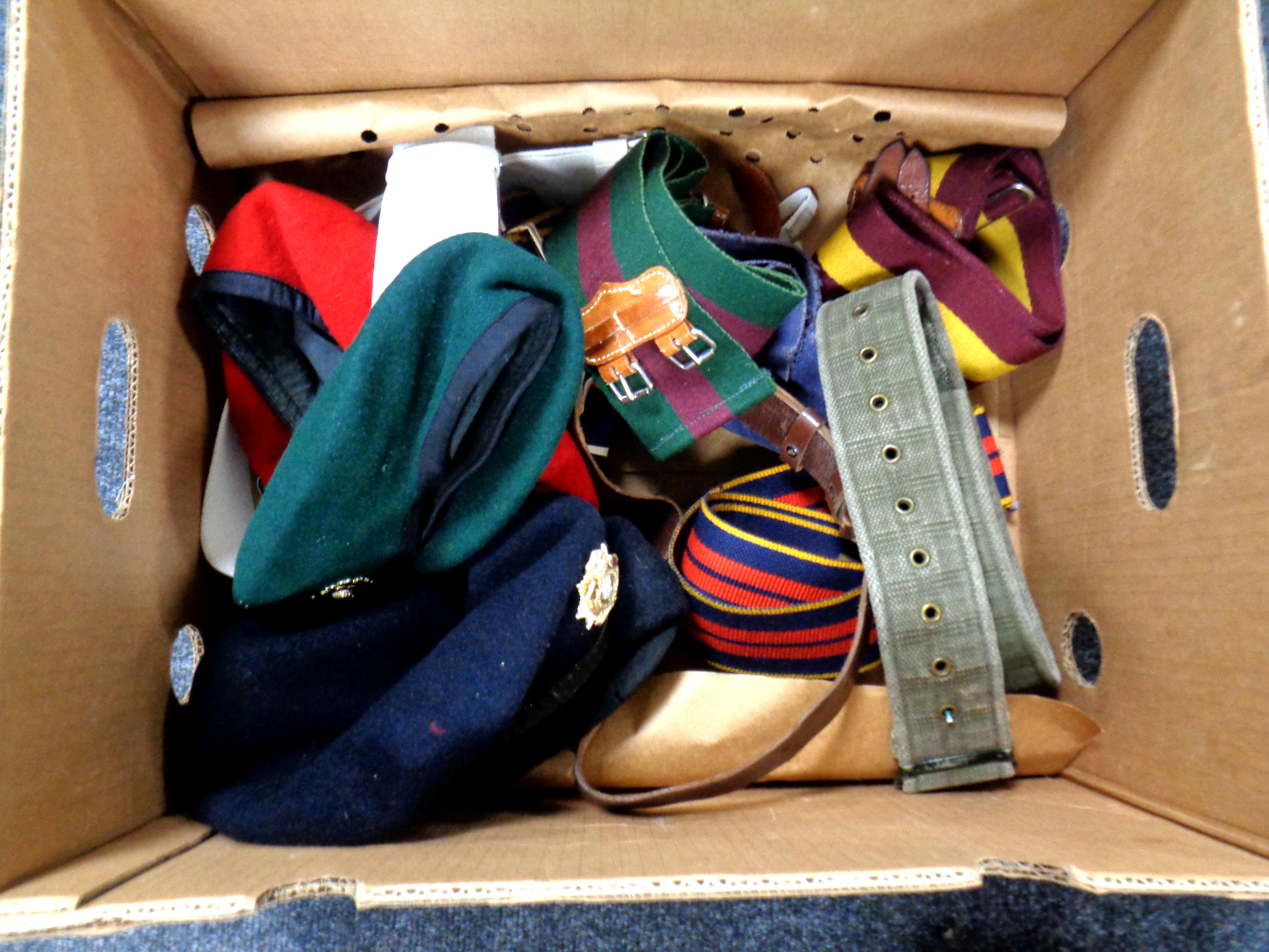 A box containing assorted army belts and berets bearing badges.