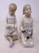 Two Nao figures, girl seated writing on a slate and girl kneeling with puppy.
