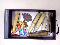 A box containing a quantity of pocket knives, enamelled badges,
