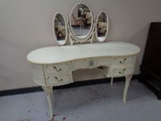 A cream and gilt knee-hole dressing table on raised legs with triple mirror.