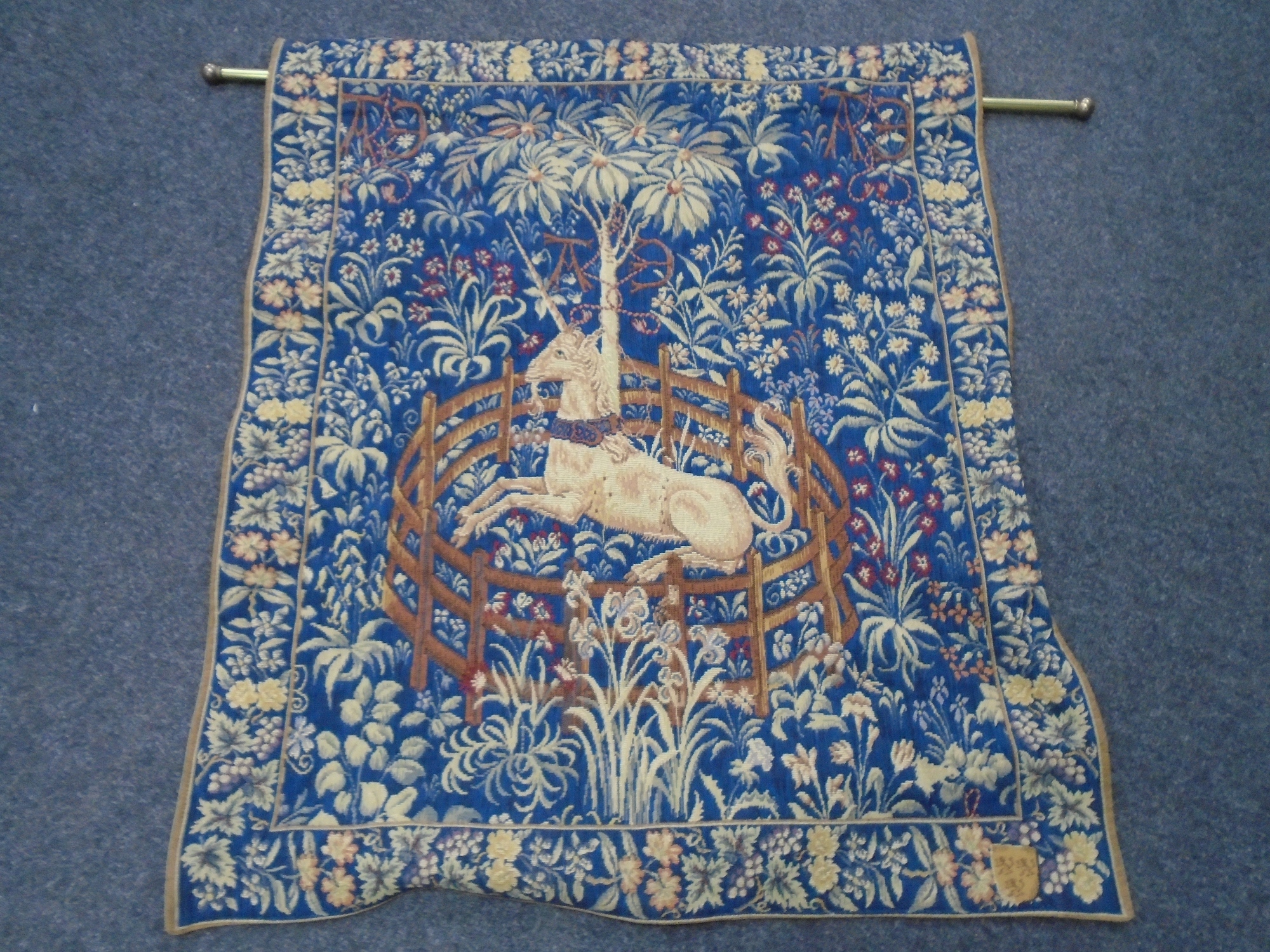 A tapestry wall hanging titled Licorne Captive, on brass pole, 96cm by 78cm.