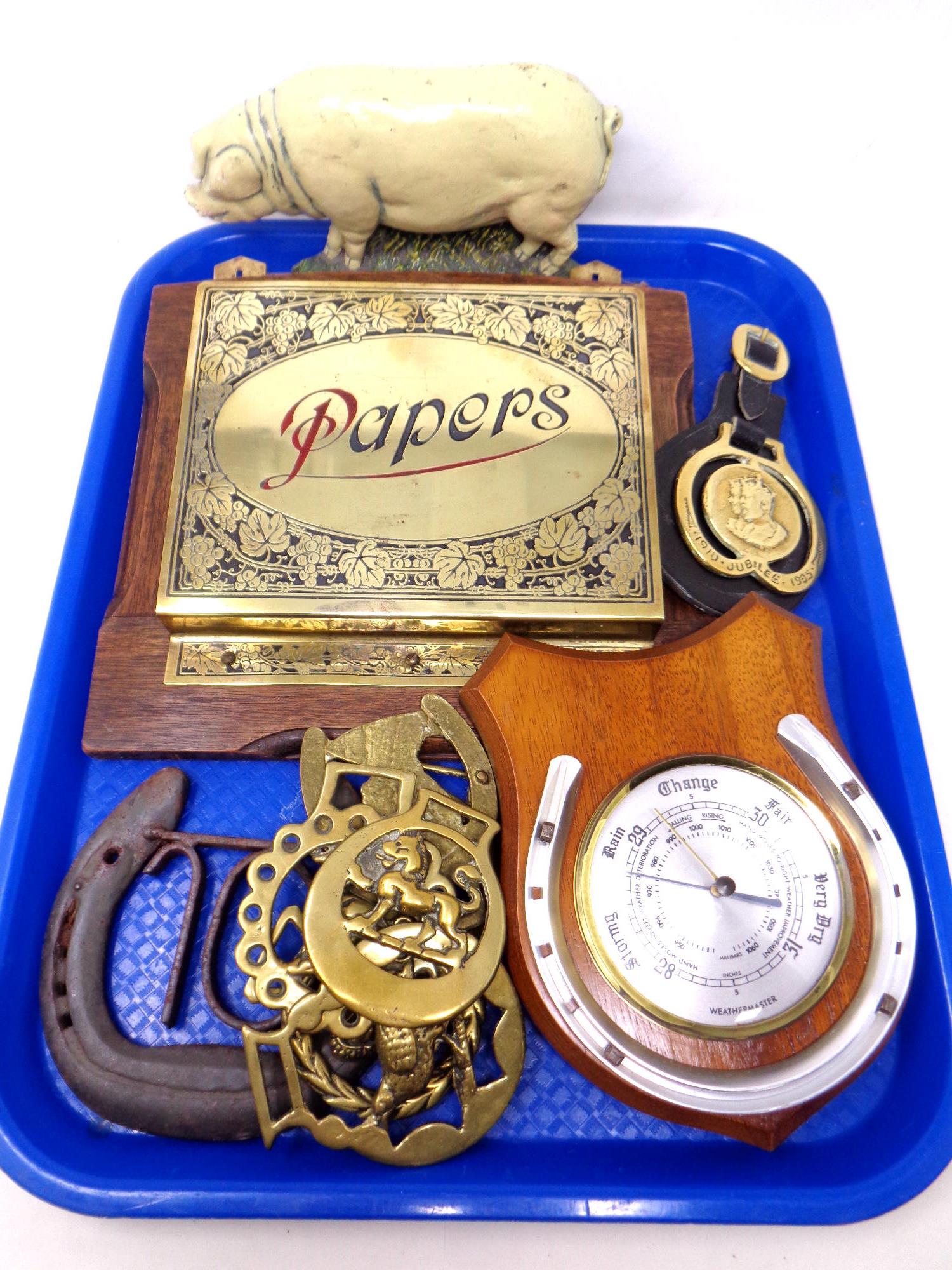 A tray containing a pig cast iron doorstop, a brass paper rack mounted on a board, horse brasses,