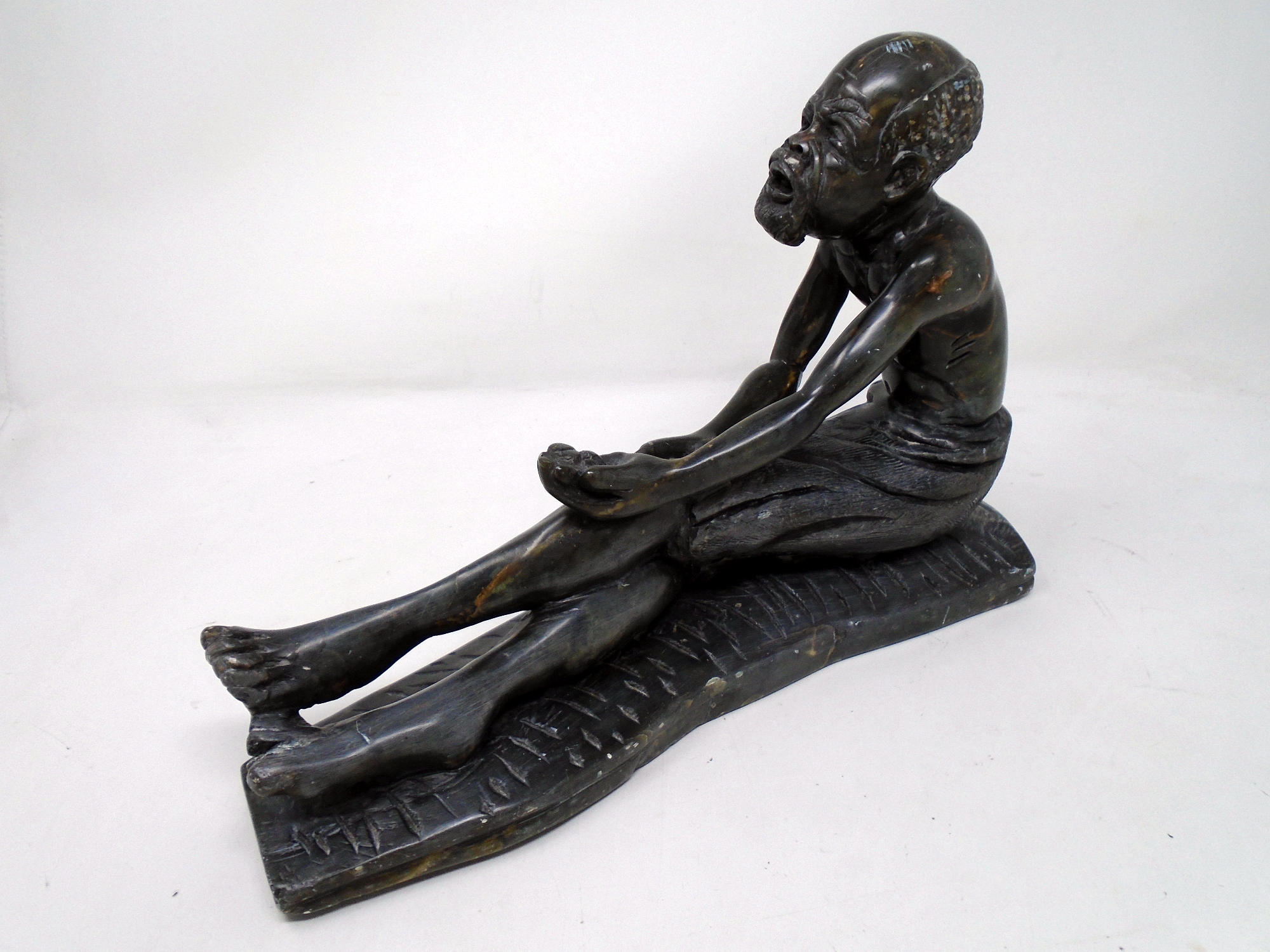 A carved African soapstone figure of a seated gentleman.