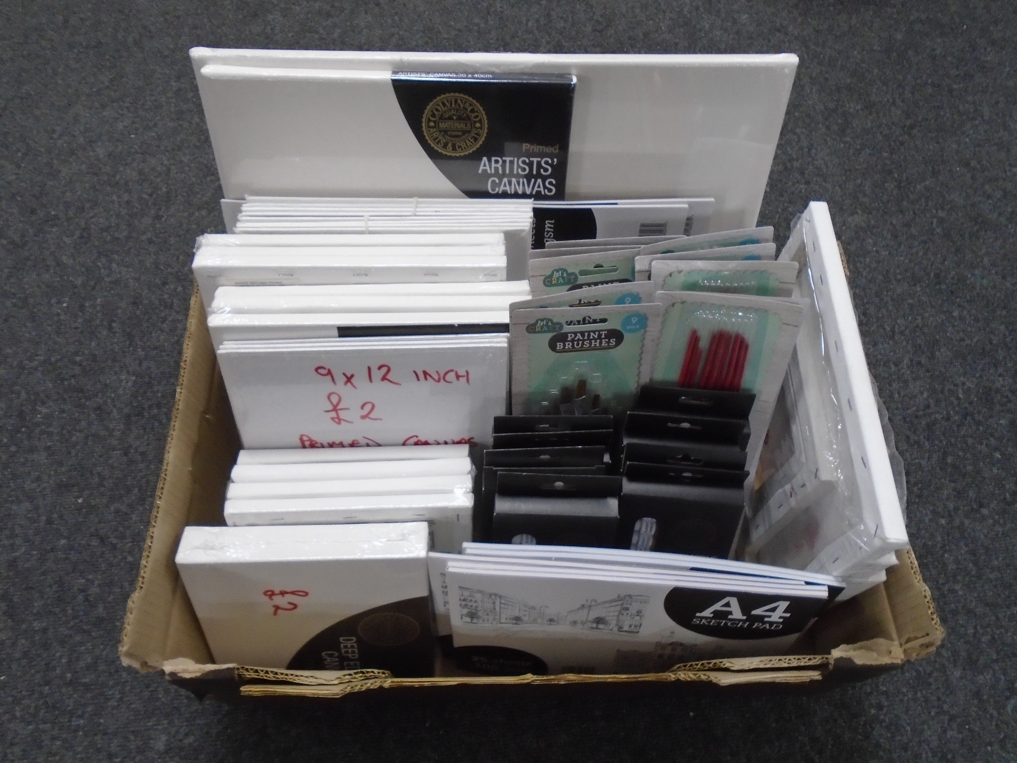 A box containing art supplies including Colvin & Co acrylic paints, canvasses, sketch pads,