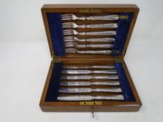 An Edwardian oak cutlery canteen containing a set of six silver plated fish knives and forks.