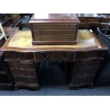 A mahogany shaped front nine drawer twin pedestal writing desk with tooled leather top