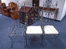 An ornate wrought iron armchair together with a further pair of high backed wrought iron chairs.